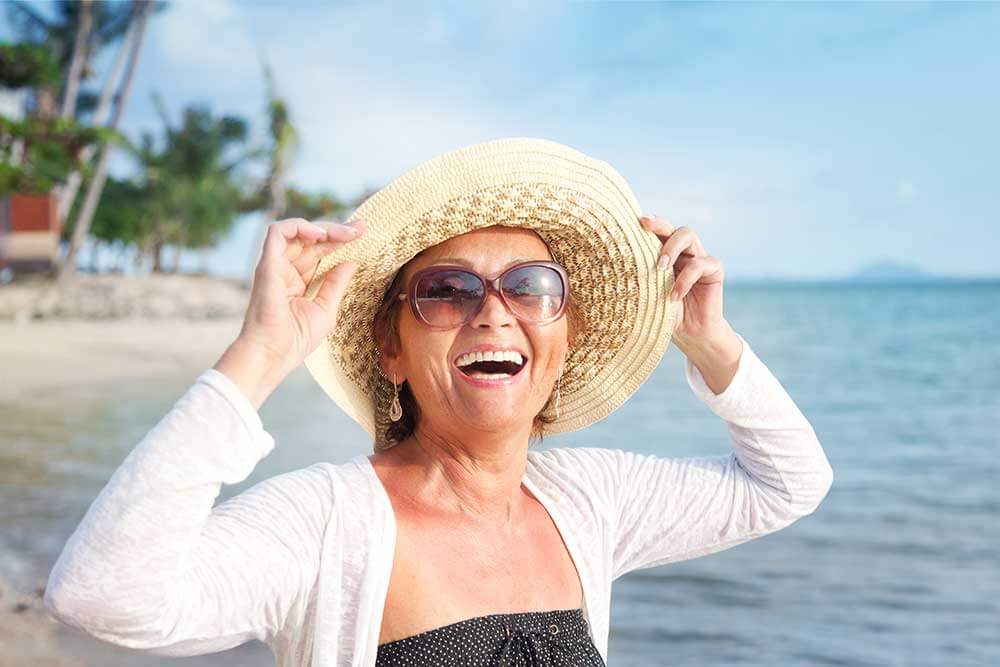 Smiling, happy woman on the beach wearing a hat and sunglasses