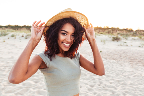 A young woman smiling on the beach wearing a hat